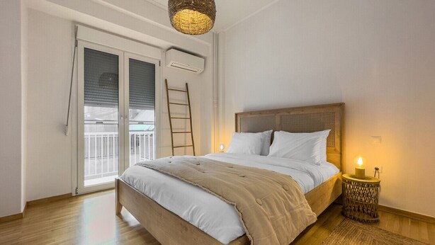 A bedroom with a wooden bed, white bedding, a small bedside table with a candle, a ladder, and a view through a large window. - Phaedrus Living: Kallithea Heights Residence (Kallithea)