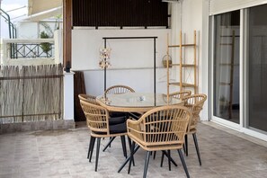 A dining area with a round glass table and wicker chairs, a hanging decoration, and a sliding glass door. - Phaedrus Living: Kallithea Heights Residence (Kallithea)