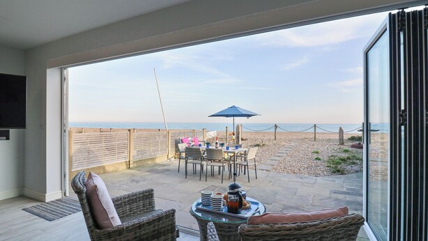 Un balcon avec des fauteuils en osier, une table avec une cafetière et une vue sur la plage.