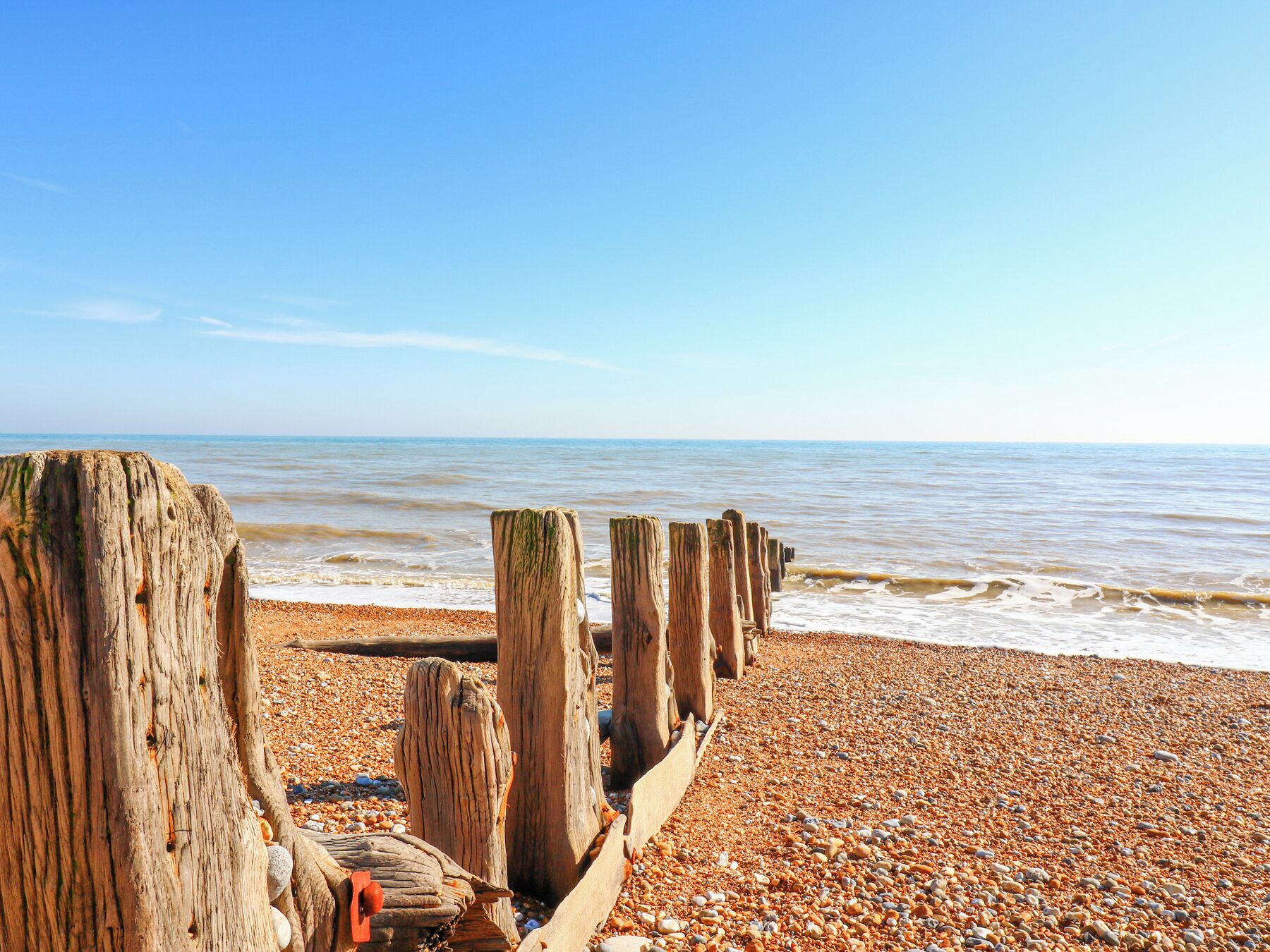 A pebbled beach with wooden posts and a clear sky.