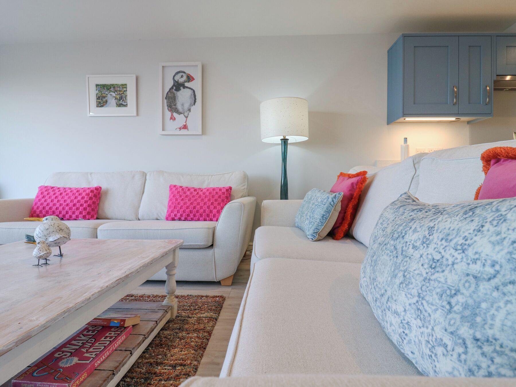 A living room with a white sofa, a coffee table, and a lamp. There are two framed pictures on the wall.