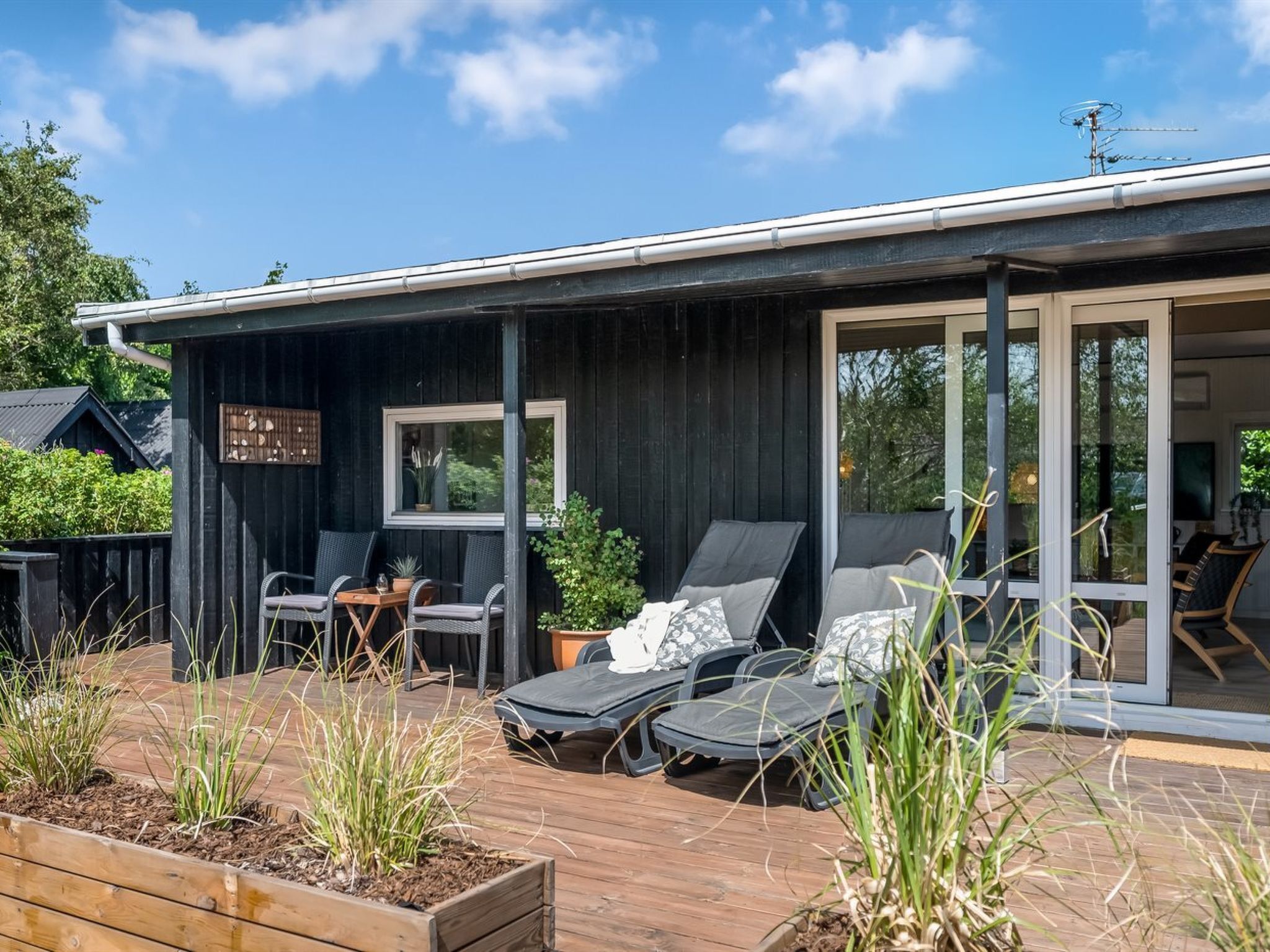 A modern outdoor deck with lounge chairs and a small table, surrounded by wooden planters and a wooden deck.