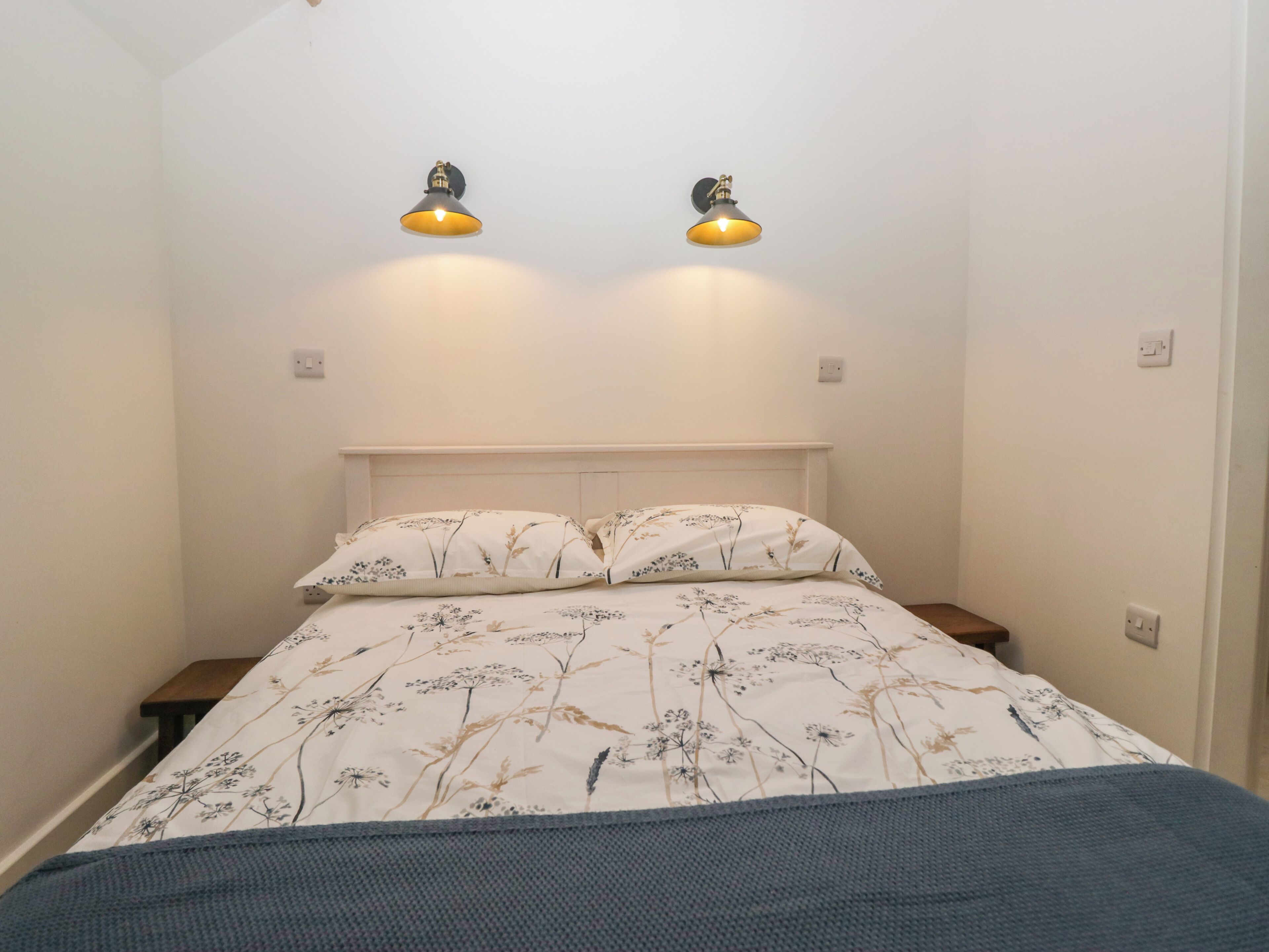 A bedroom with a bed, two wall-mounted lights, and a nightstand.