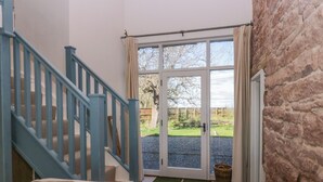 A room with a staircase, a door leading outside, and a view of a garden. - The Roost (Carlisle)