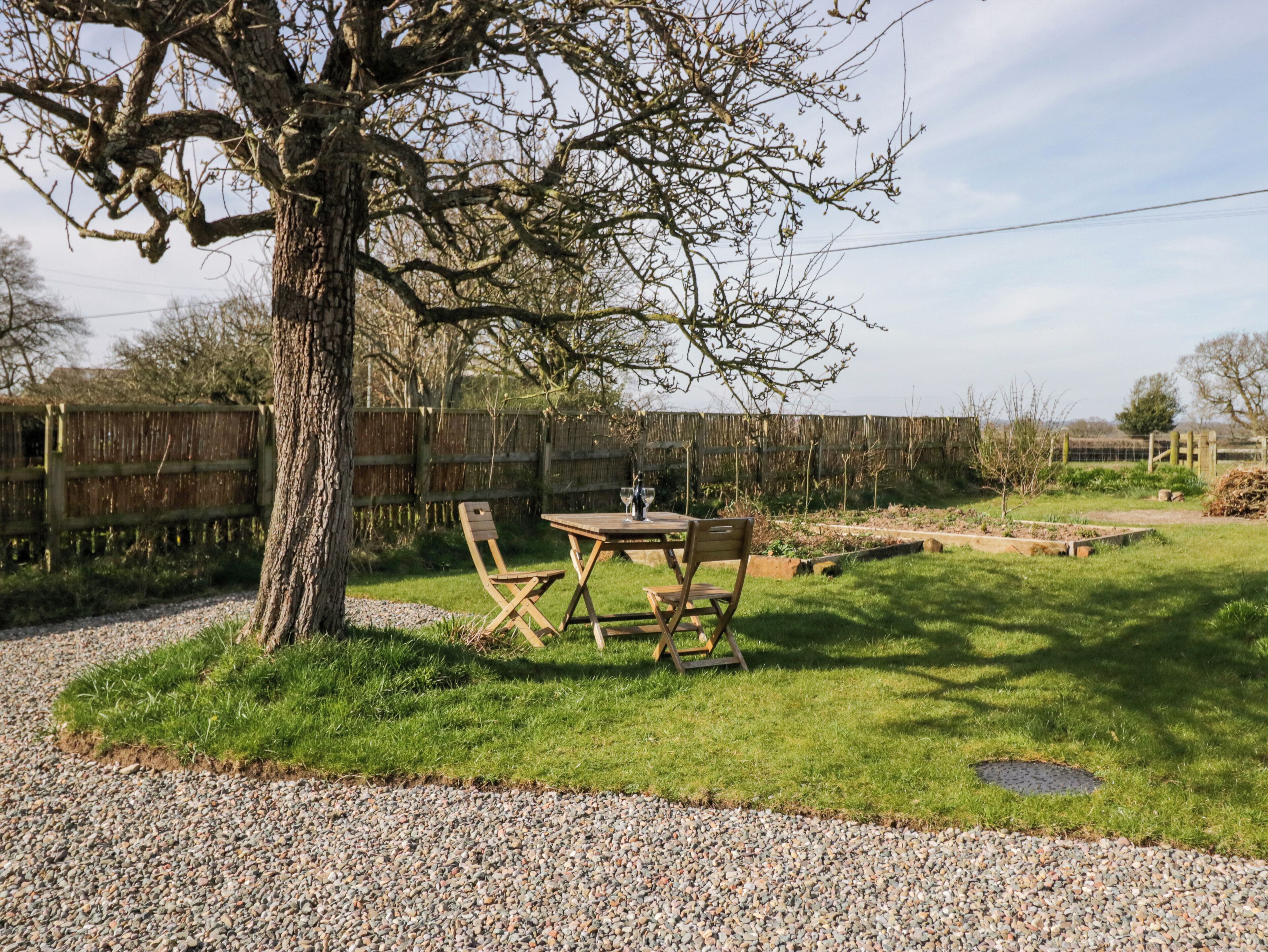 An outdoor seating area with a table and chairs, surrounded by a grassy lawn and a wooden fence.