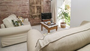 A cozy living room with a brick wall, a wooden door, a sofa, a coffee table with a tray, and a potted plant. - The Roost (Carlisle)