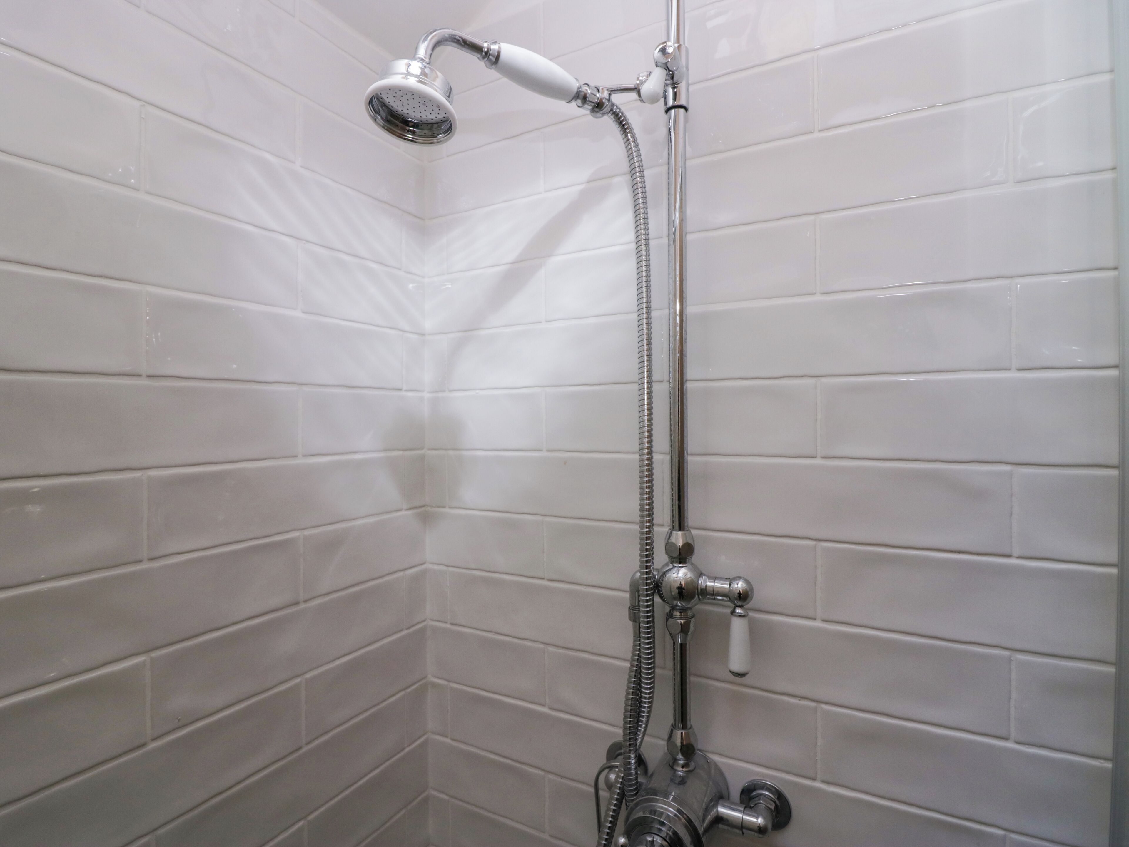 A shower with a handheld showerhead and a flexible hose, mounted on a wall with white tiles.