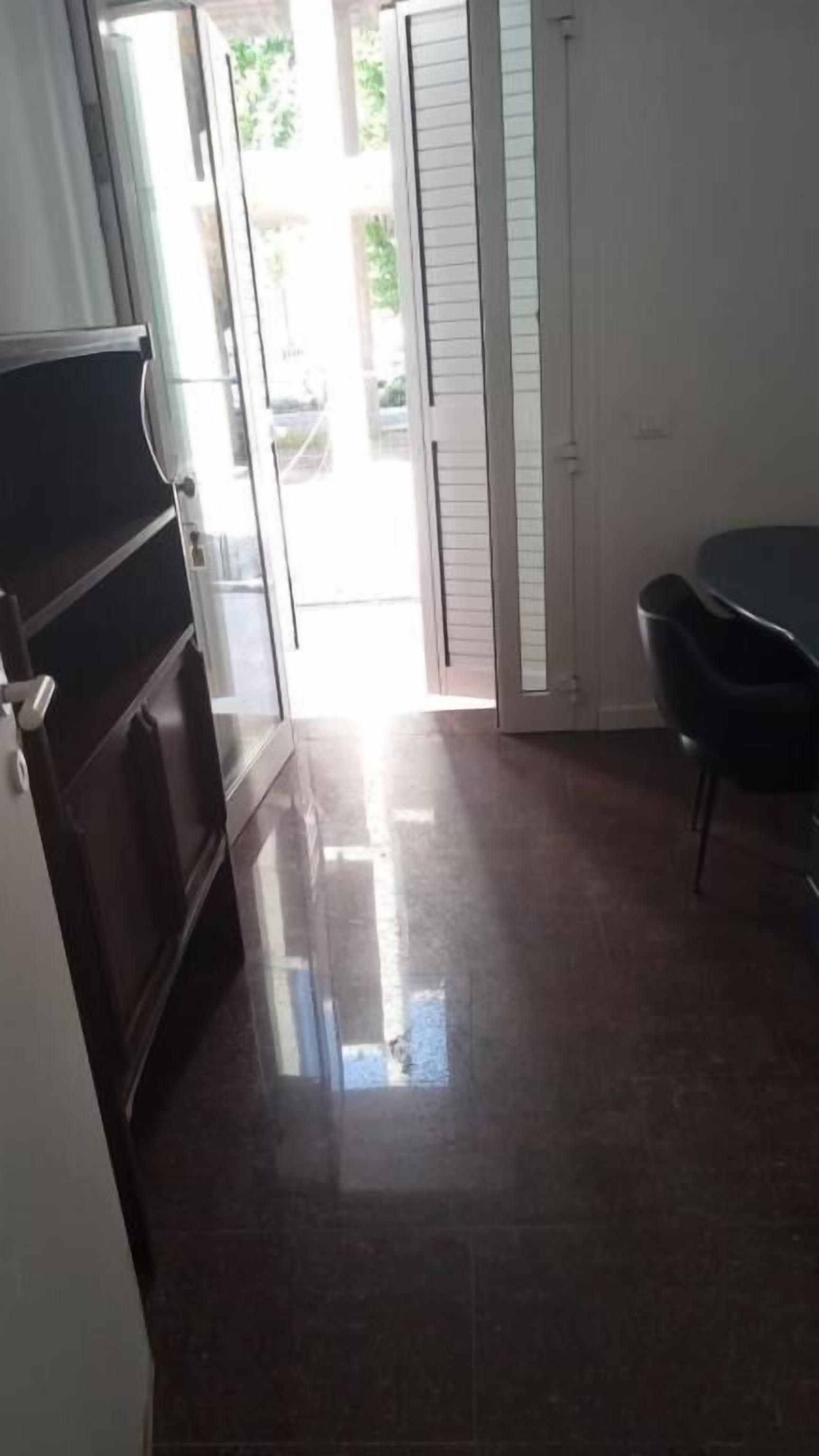 Une pièce dotée d’une porte-fenêtre coulissante donnant sur un espace extérieur, d’un canapé de couleur sombre et d’une petite table avec une chaise.
