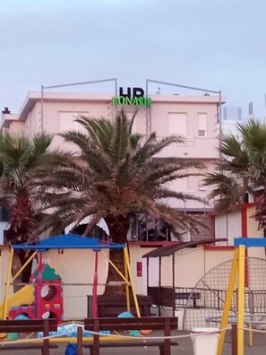 A playground with colorful equipment and a palm tree in the foreground. - Hotel Bonaria sul mare (Rimini)