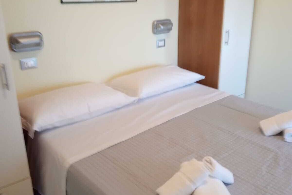 Una cama bien hecha con sábanas blancas y dos toallas enrolladas sobre la cama.