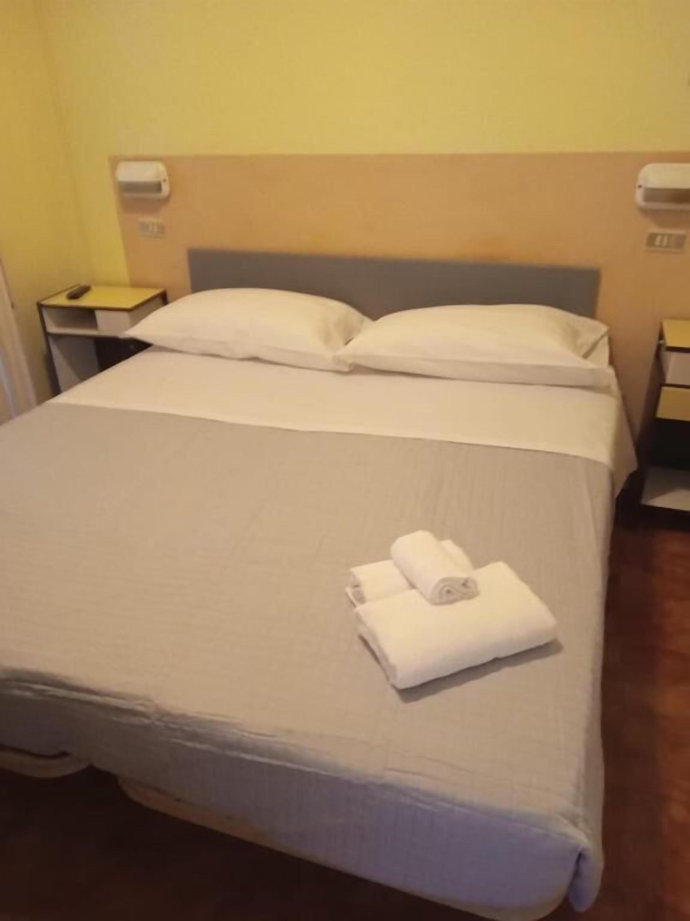 Una cama bien hecha con sábanas blancas y dos toallas enrolladas en el reposapiés.
