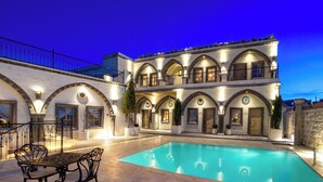 Un hotel con piscina, area salotto all'aperto e un edificio a più piani caratterizzato da finestre ad arco e balconi.