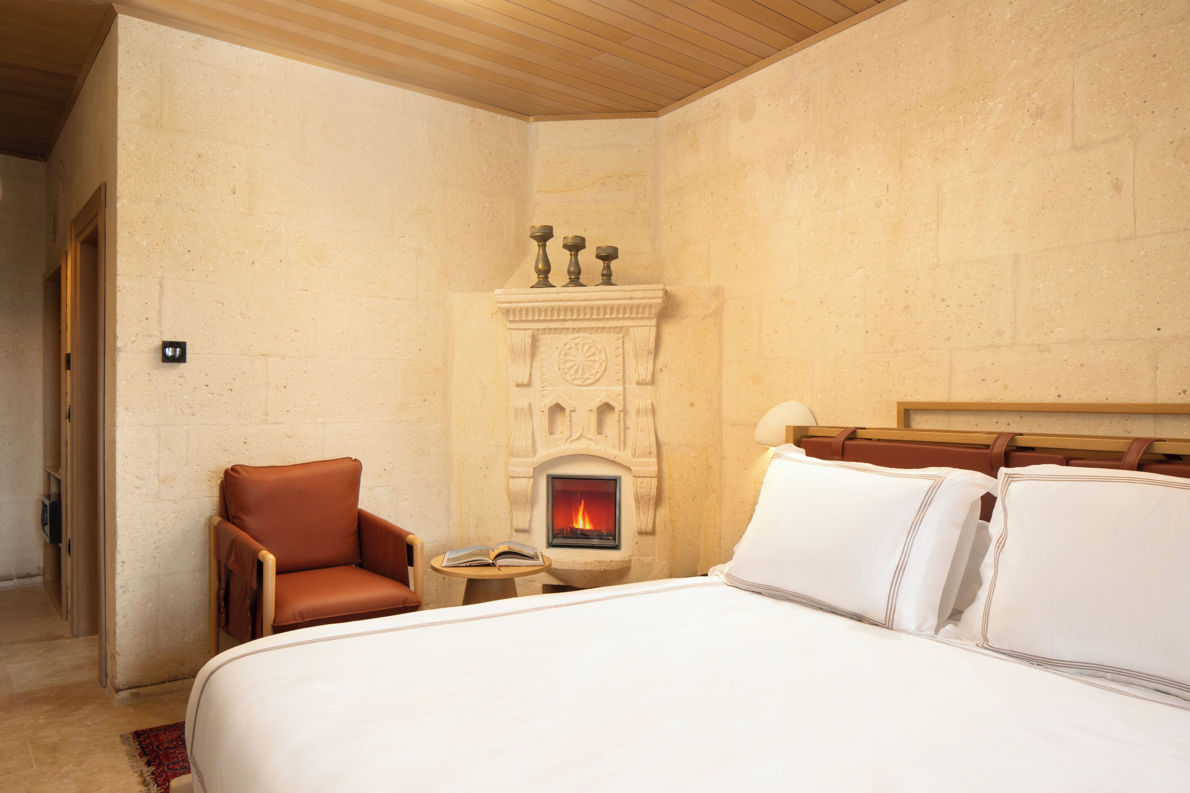 A bedroom with a fireplace, a bed, a chair, and a small table with a book.