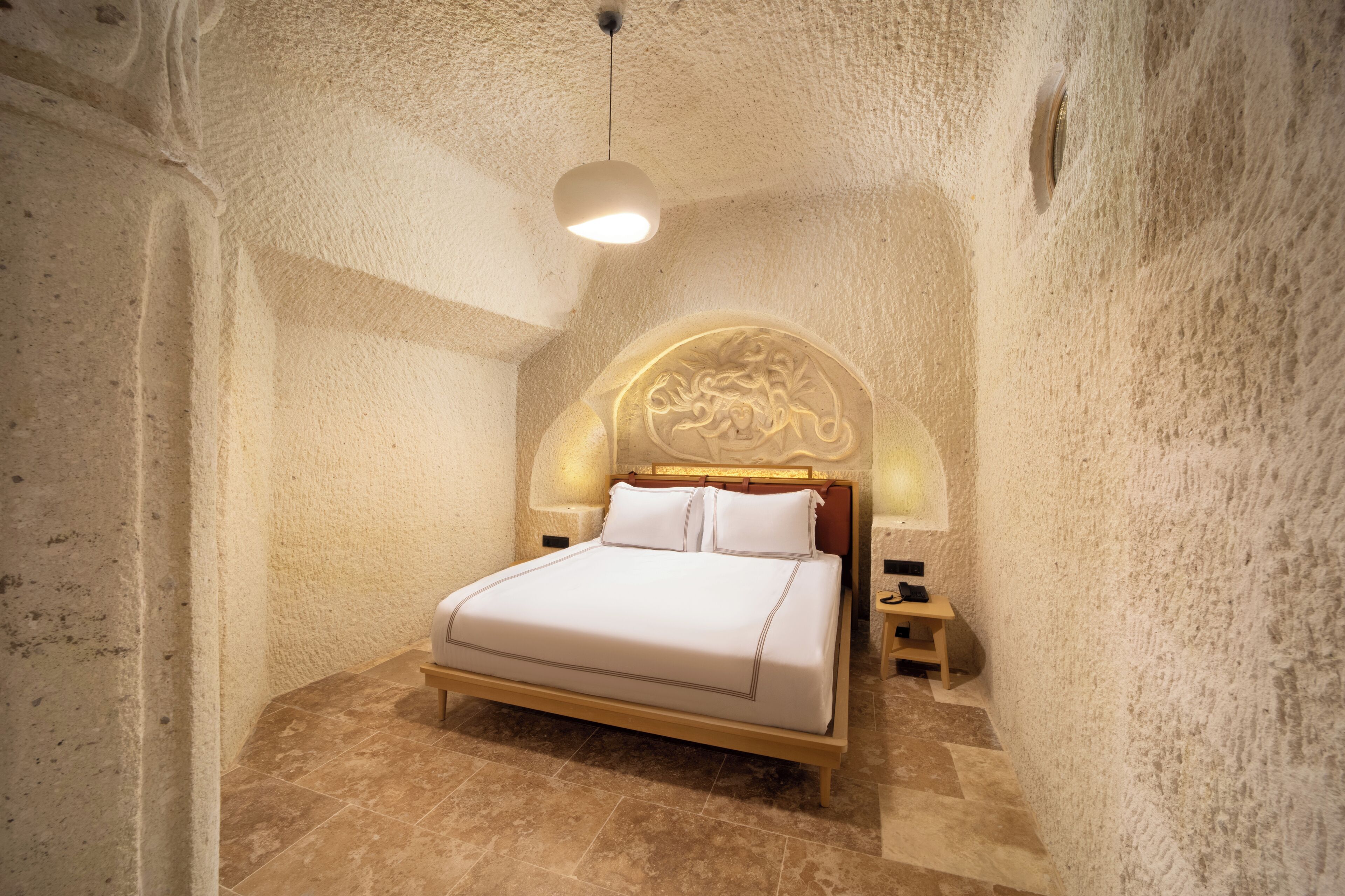 Un dormitorio con cama, mesita de noche, lámpara de pared y cabecero decorativo.