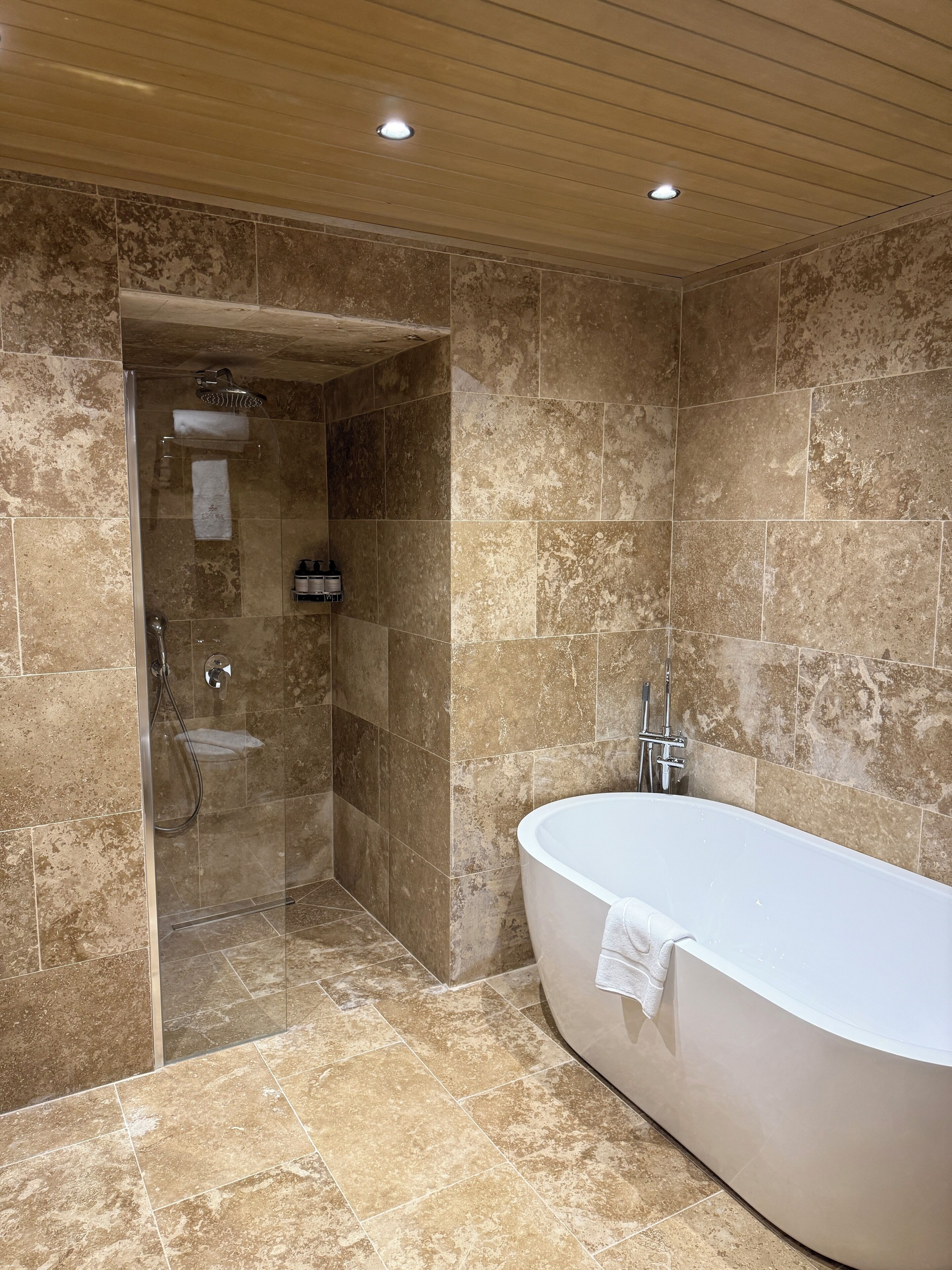 A modern bathroom with a glass-enclosed shower, a freestanding bathtub, and tiled walls.