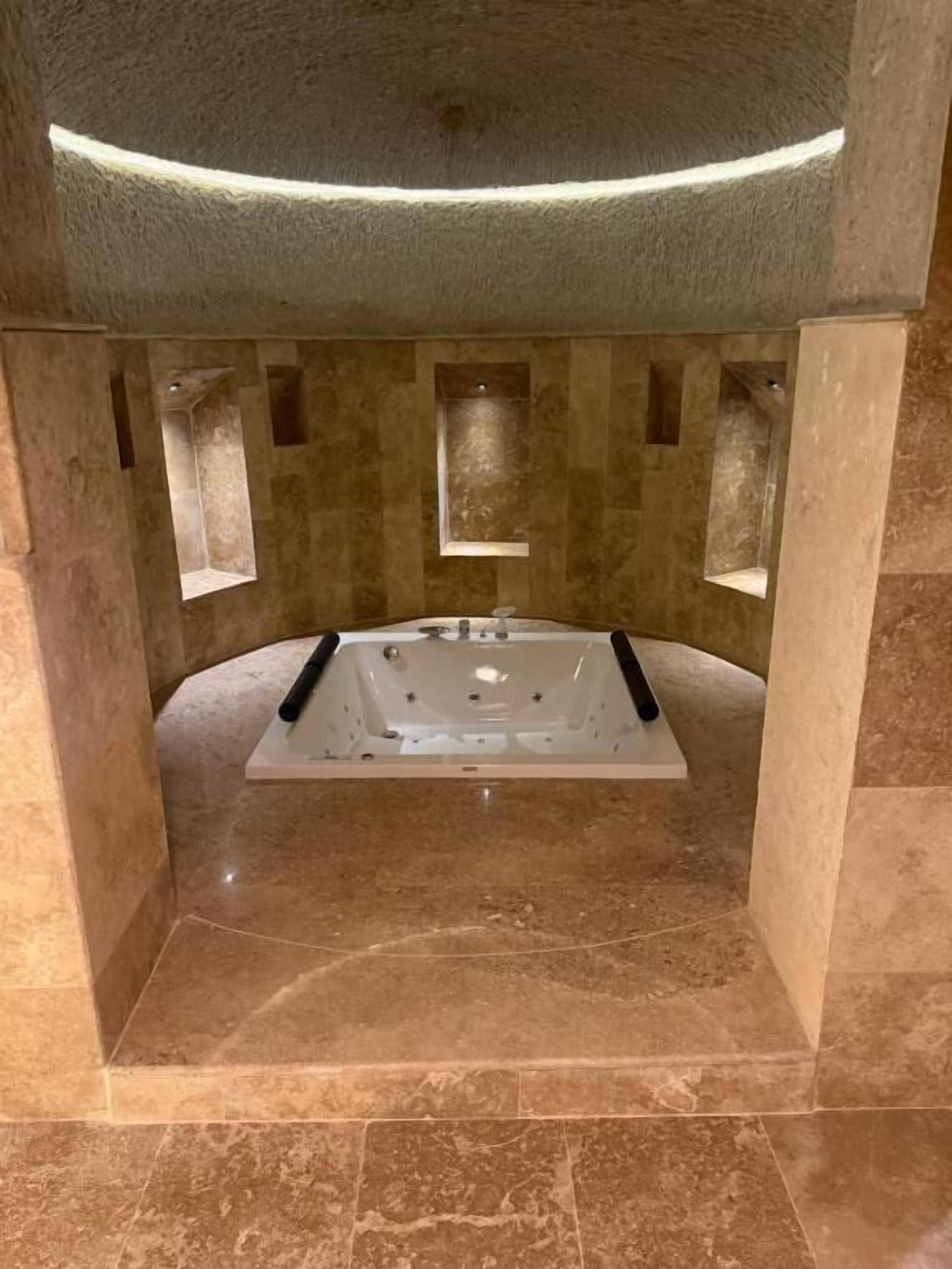 A modern bathroom with a freestanding bathtub, marble walls, and a recessed lighting fixture.
