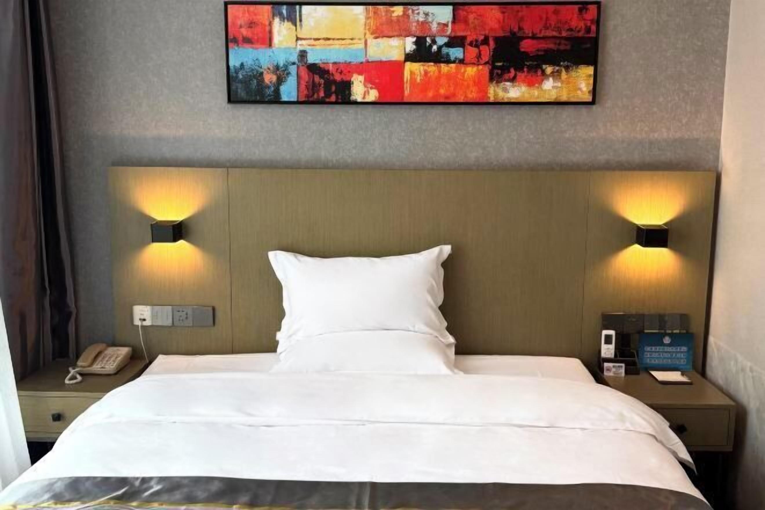 A hotel room with a large bed, two bedside lamps, a nightstand with a phone, and a wall-mounted abstract painting.