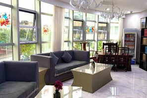 A modern living room with a sofa, coffee table, and chairs. There are large windows with curtains, a chandelier, and a bookshelf. - Shanyehong Hotel (Beijing)