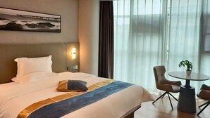 A hotel room with a bed, a desk, a chair, a plant, and a window with curtains. - Shanyehong Hotel (Beijing)