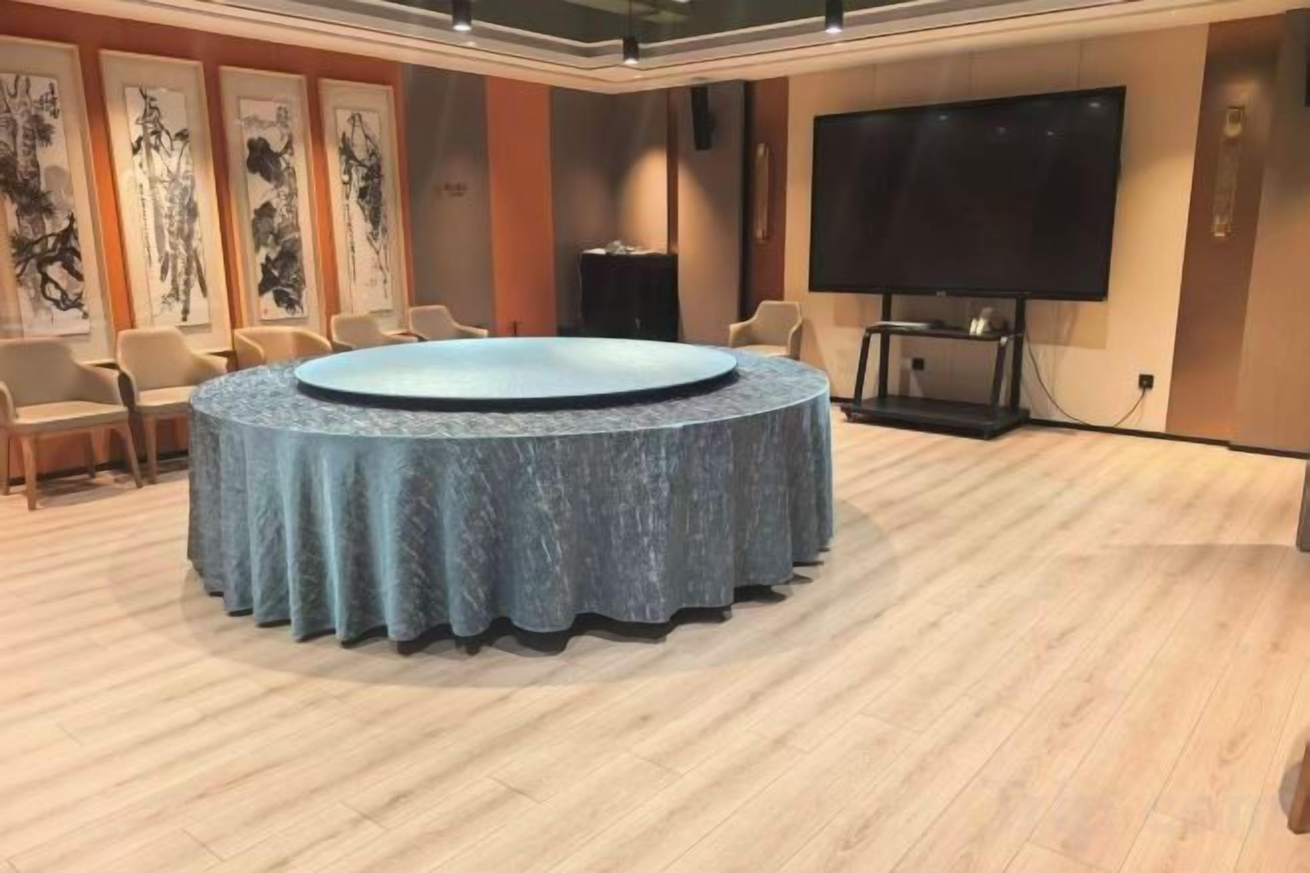 Un salón de conferencias con una mesa redonda, sillas, una pantalla grande y obras de arte en las paredes.