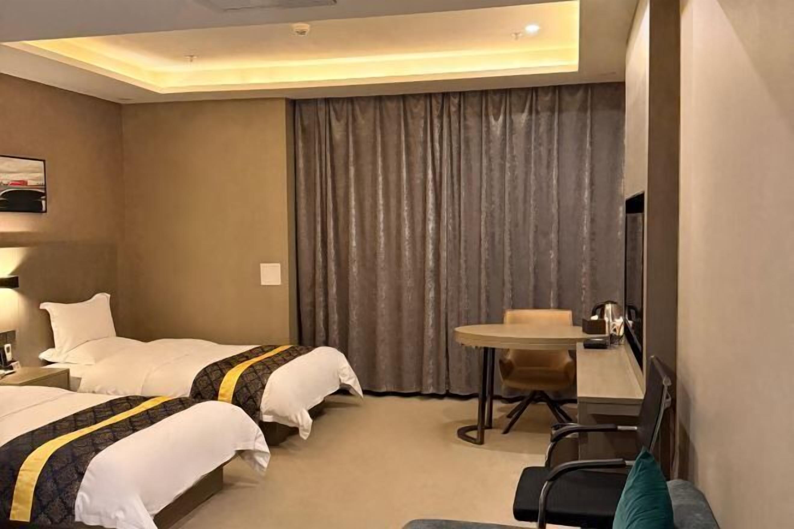 A hotel room with two beds, a desk, a chair, and a large window with curtains.