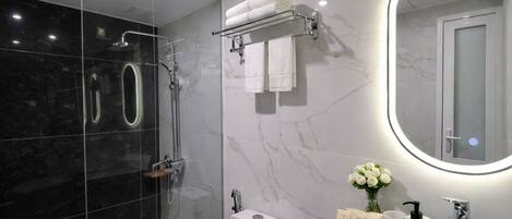 Un baño moderno con ducha de vidrio, lavamanos blanco y tocador con artículos de aseo.