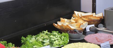 A buffet with various food options including salads, bread, and sliced meats.
