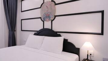Quarto de hotel com cama, mesa de cabeceira com abajur, uma obra de arte na parede e janela com cortinas.