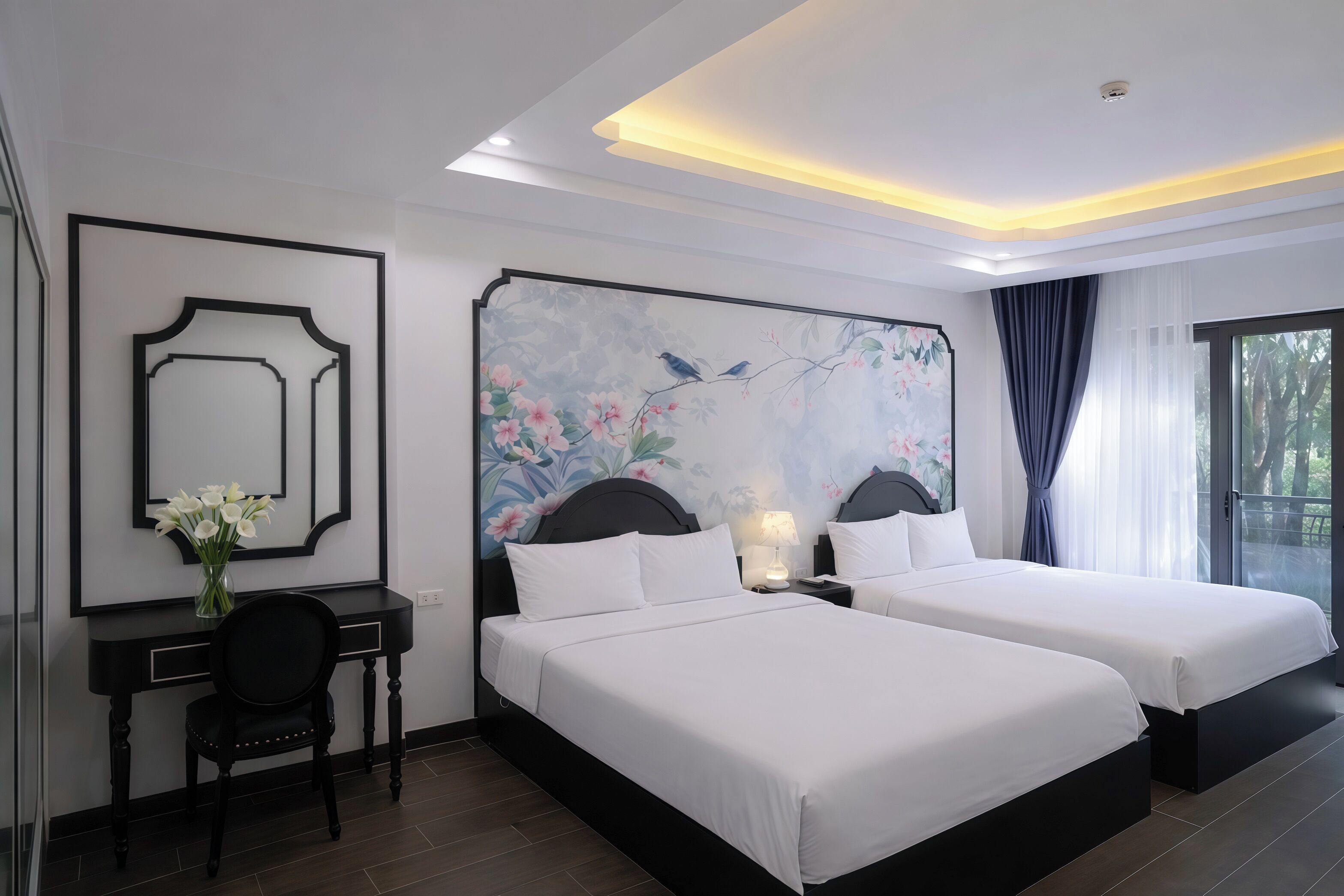 Habitación de hotel con dos camas, un escritorio y una silla, un cuadro grande con motivos florales en la pared, y una ventana con cortinas.