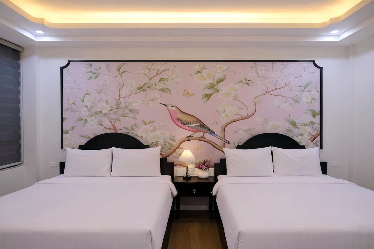 A hotel room with two beds, a nightstand with a lamp, and a wall mural of a bird on a branch.