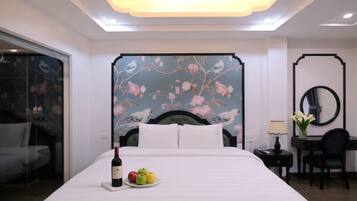 A hotel room with a large bed, a desk with a chair, a mirror, and a wall with floral wallpaper.