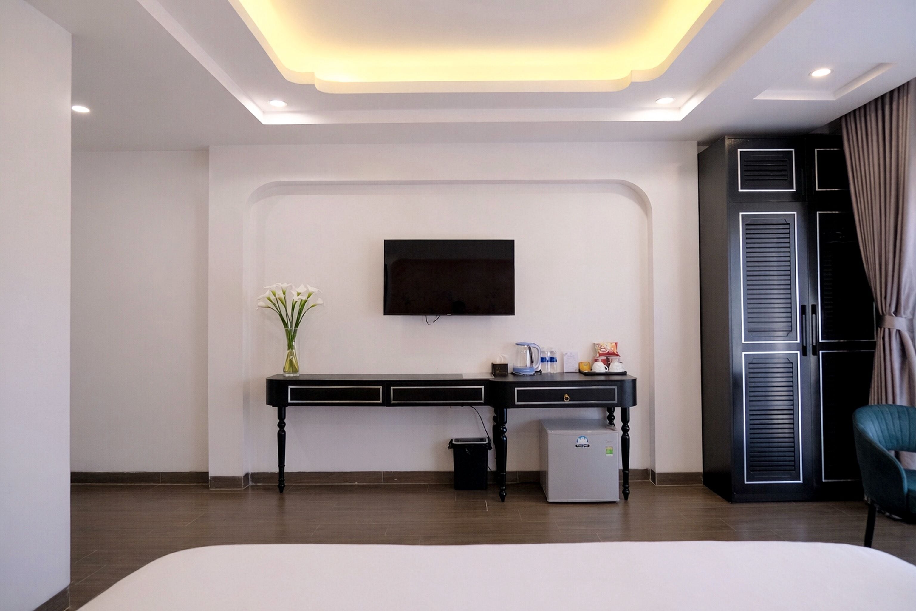 Una habitación de hotel moderna con una televisión de pantalla plana montada en la pared, un escritorio pequeño con una cafetera, un cubo de basura y un refrigerador miniatura.
