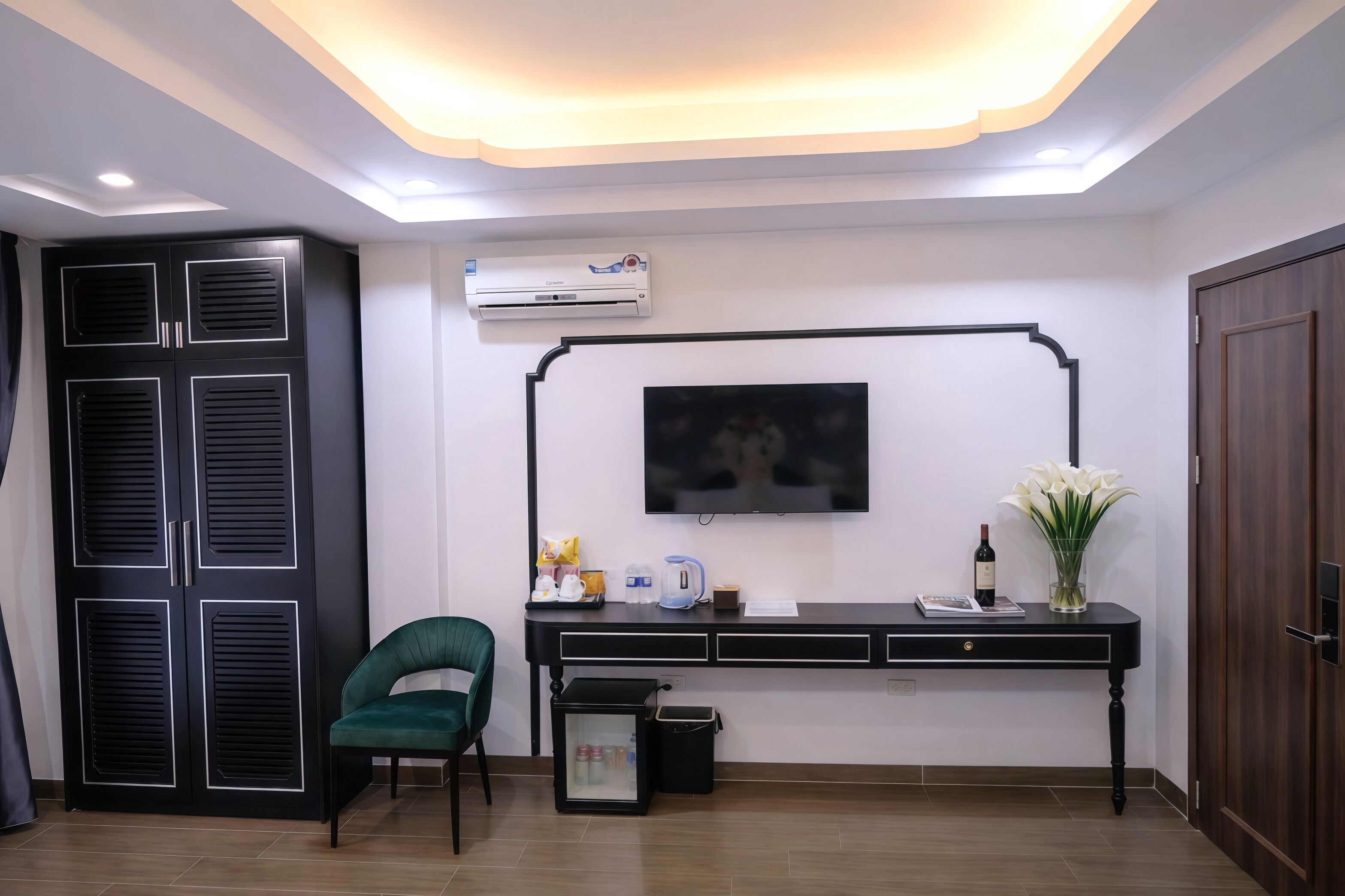 A modern room with a black wardrobe, a desk with a flat-screen TV, a green chair, and a small trash bin.