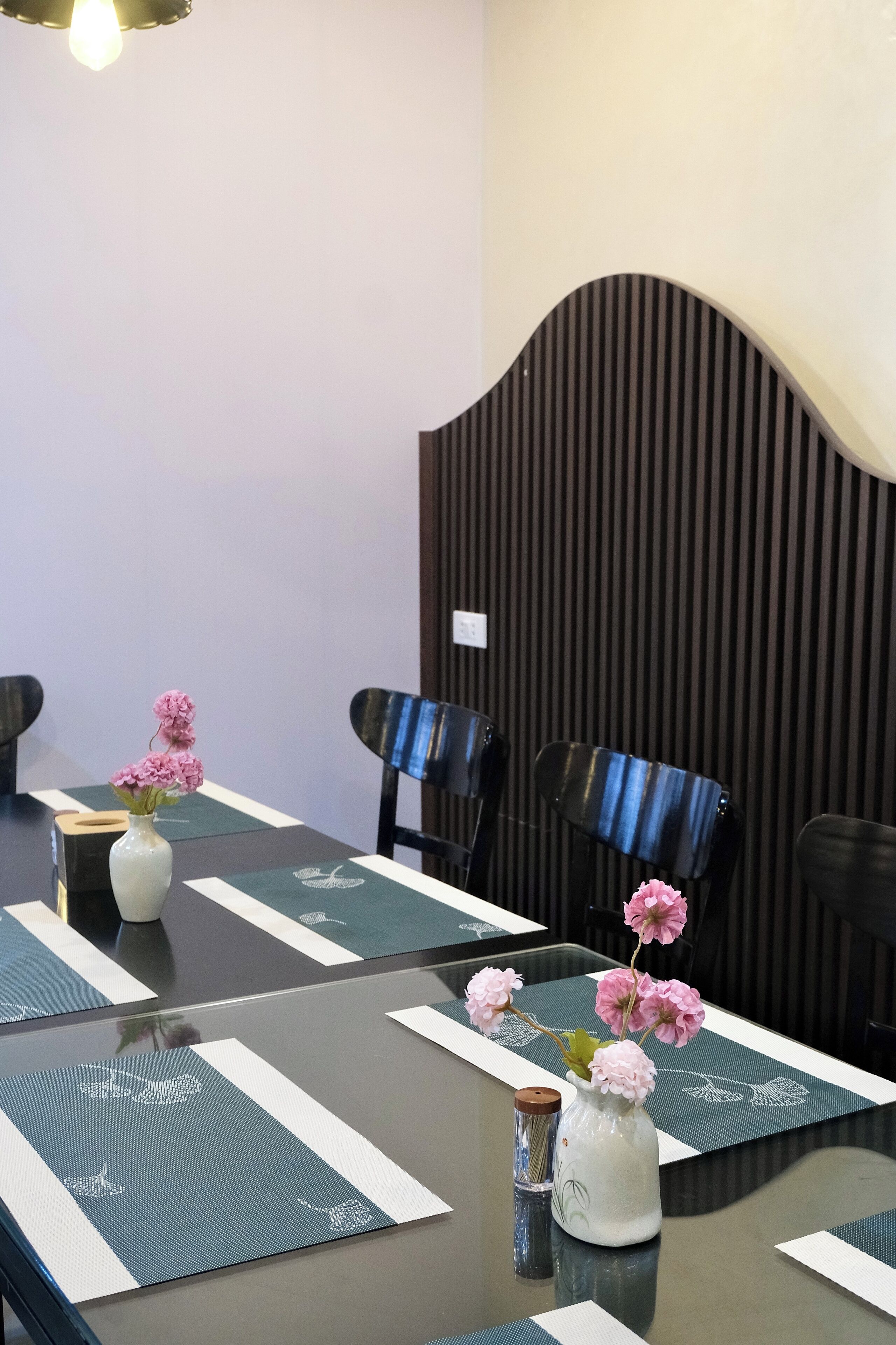 A conference room with a glass table, black chairs, and a white vase with pink flowers.