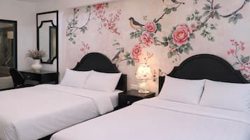 A hotel room with two beds, a nightstand with a lamp, a mirror, and a wall with floral and bird artwork.