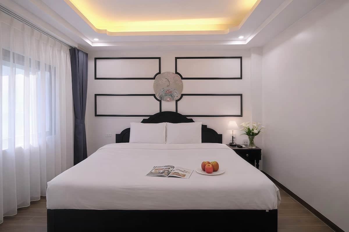 A neatly made bed with a magazine, a plate of fruit, and a vase of flowers on a bedside table.