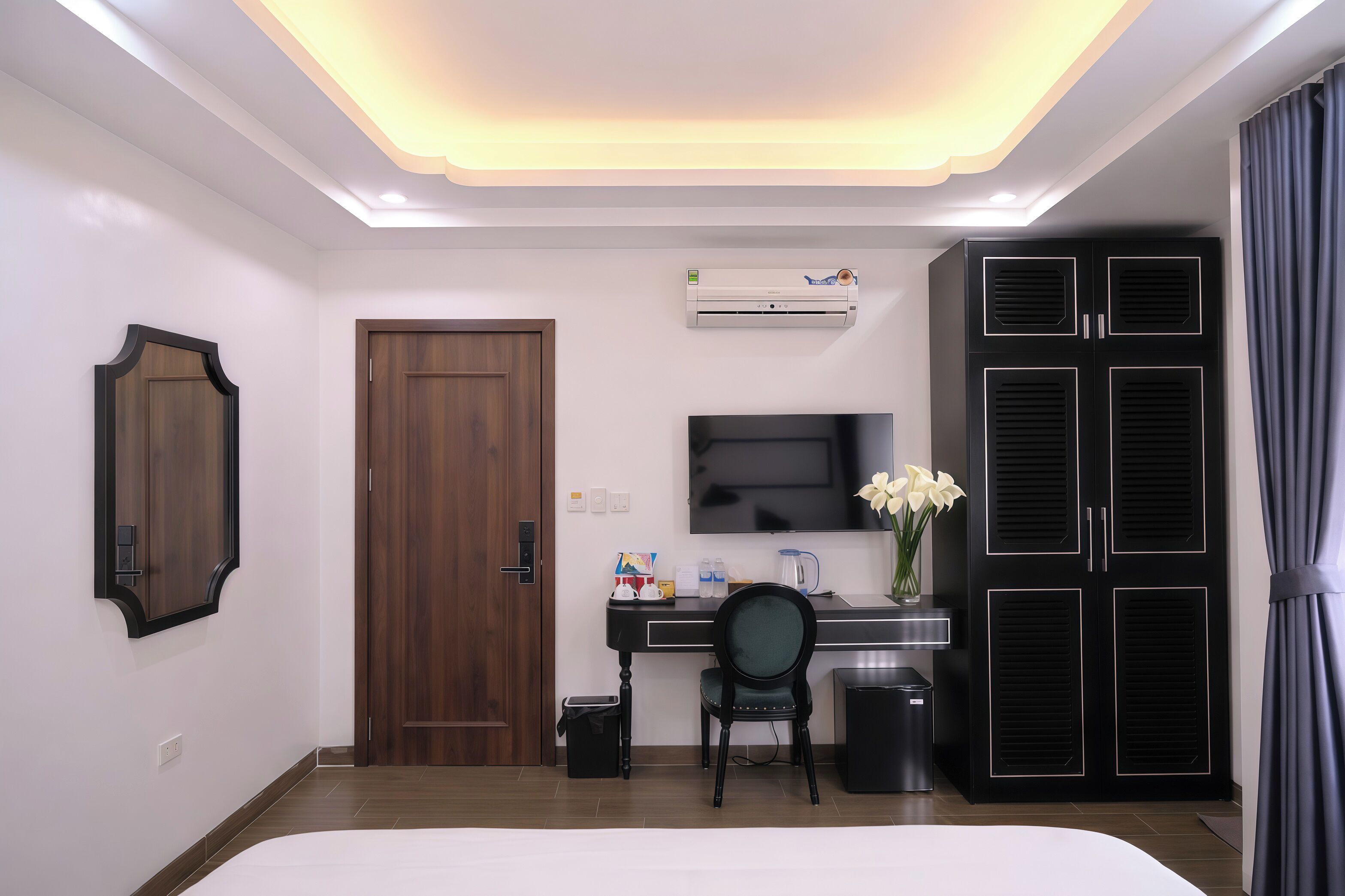 A hotel room with a bed, a desk with a chair, a TV, an air conditioner, and a wardrobe.
