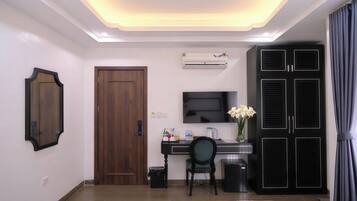 A hotel room with a bed, a desk with a chair, a TV, an air conditioner, and a wardrobe.