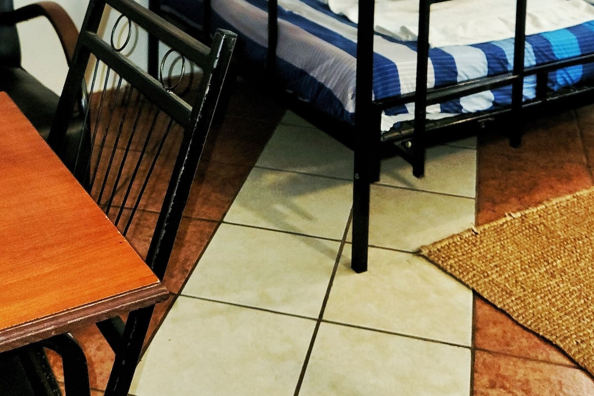 Ein Stockbett mit blauen und weißen Streifen, ein Holztisch mit einem Stuhl und ein gefliestes Badezimmer.