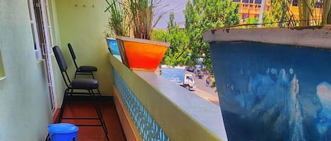 A balcony with a red floor, a blue trash bin, a black chair, and a potted plant.