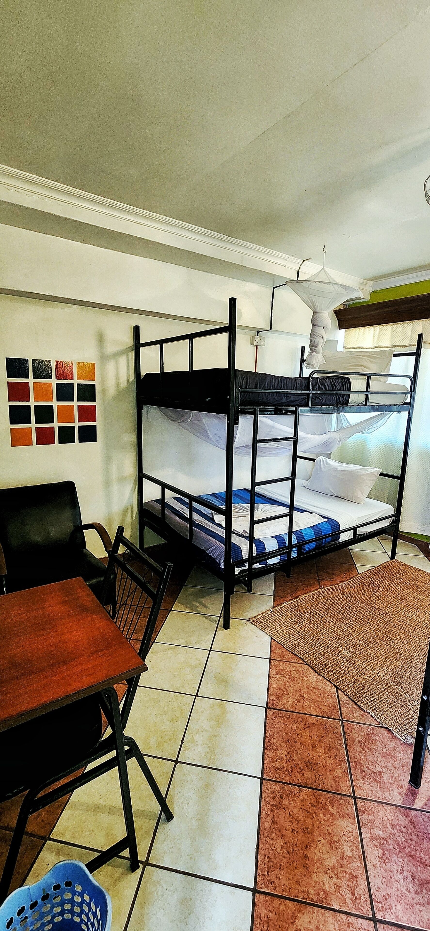 A dormitory room with bunk beds, a desk, chairs, and a tiled floor.