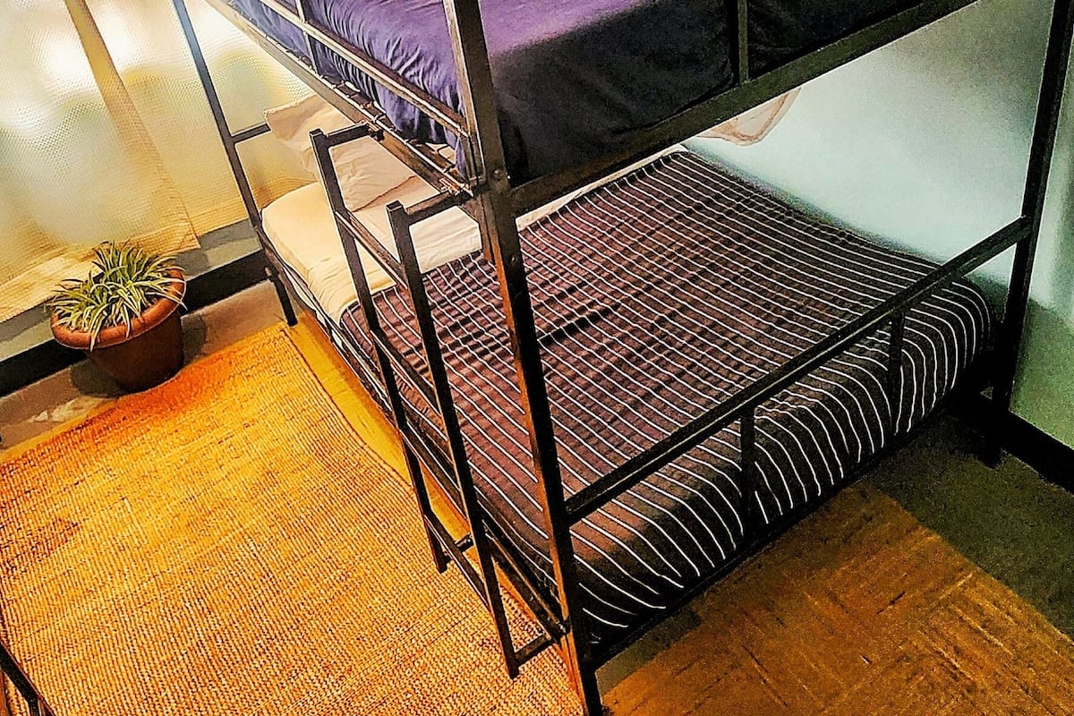 Ein Stockbett mit Moskitonetz, ein Topf mit Pflanze und eine gewebte Matte auf dem Boden.