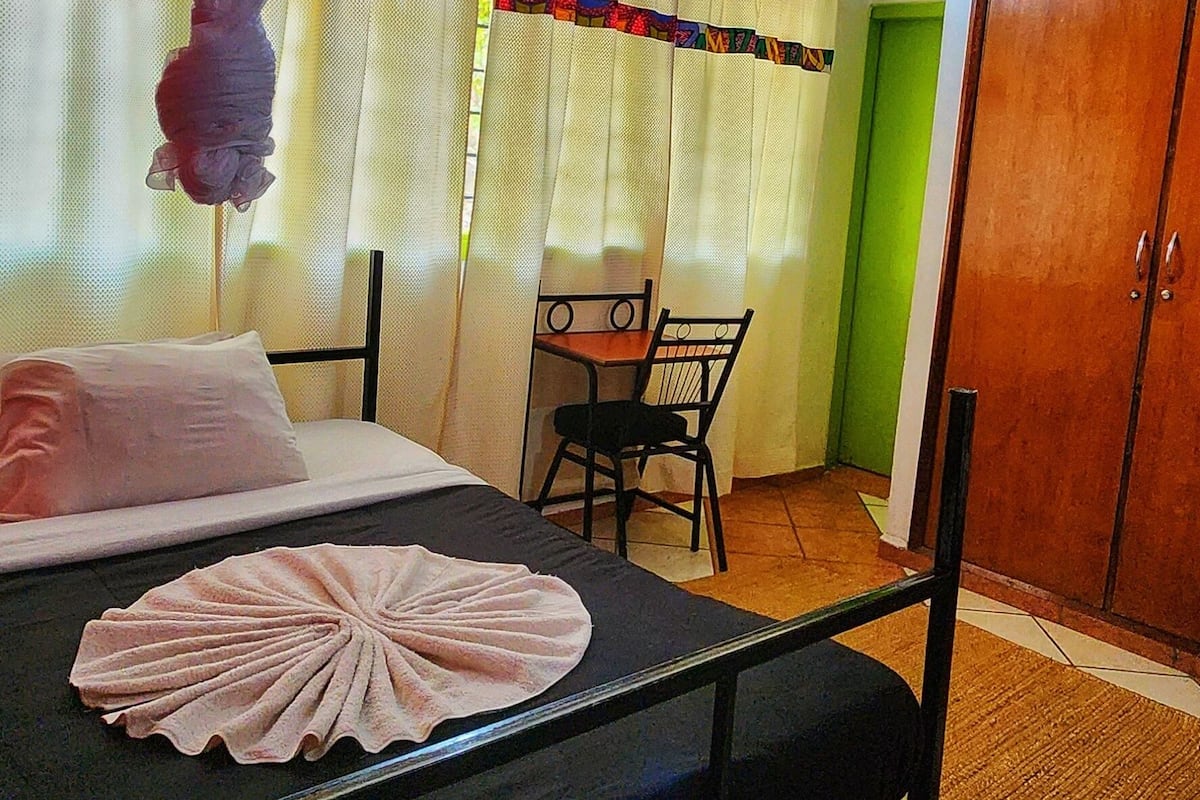 Ein Hotelzimmer mit Bett, Moskitonetz, Stuhl, Tisch und Kleiderschrank.