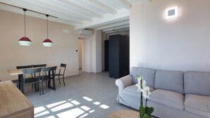 Een moderne woonkamer met een bank, een eettafel met stoelen, hanglampen en een potplant.