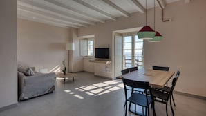 Een moderne woonkamer met een bank, een eettafel met stoelen, een televisie en een raam met natuurlijk licht.