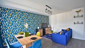 Un salon moderne avec un canapé bleu, une table à manger avec des chaises et un coin cuisine équipé de placards et d’un téléviseur.