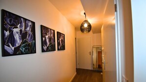 Un couloir avec trois tableaux abstraits encadrés accrochés au mur, un luminaire suspendu et une porte au fond.