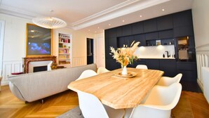 A modern living room with a wooden dining table, white chairs, a sofa, and a black accent wall with built-in shelves. - Paris Pantin Prestige (Pantin)