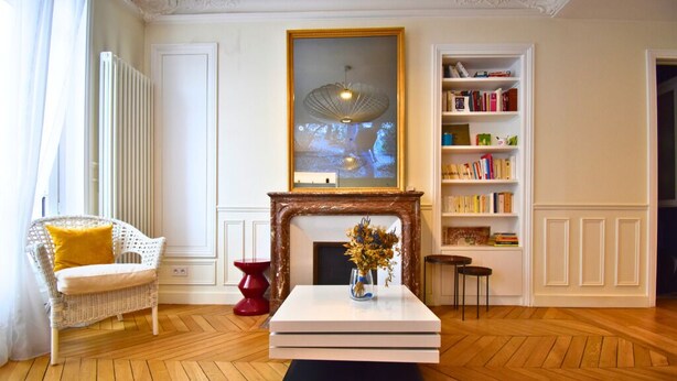 A living room with a white fireplace, a bookshelf, a wicker chair, and a red stool. - Paris Pantin Prestige (Pantin)