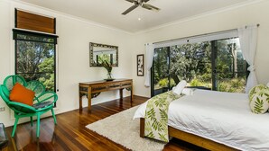 Quarto com cama, poltrona, escrivaninha e uma grande janela.